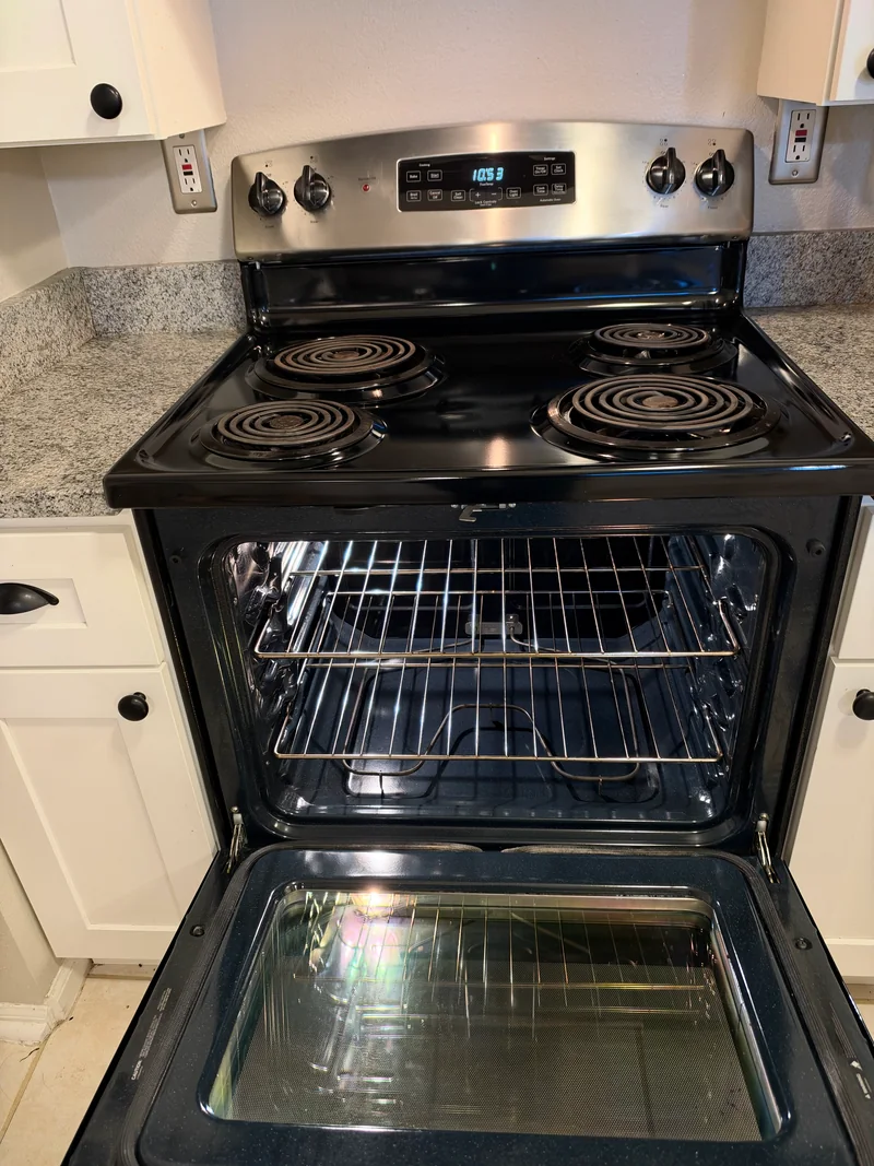 Clean black stovetop and open oven with racks and glass door